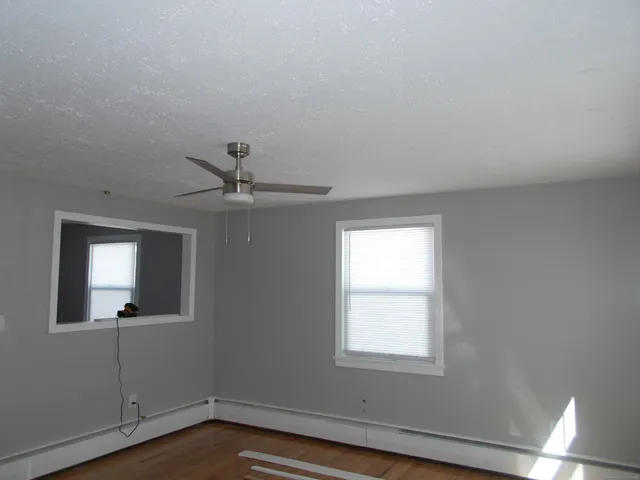 an empty room with wooden floor chandelier fan and windows