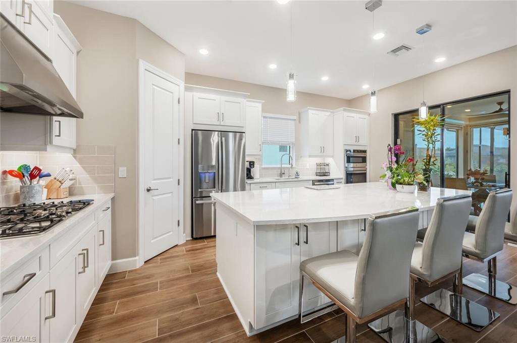 8416 Rosa Court Naples, FL 34114 - Photo 8 of 34 Open-concept kitchen featuring an expansive central island with seating, white shaker cabinetry, stainless steel appliances, and wood-finish flooring