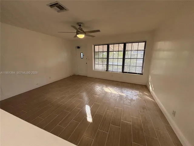 an empty room with wooden floor fan and windows