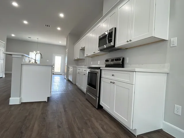 a kitchen with stainless steel appliances granite countertop a stove top oven a sink dishwasher and white cabinets with wooden floor