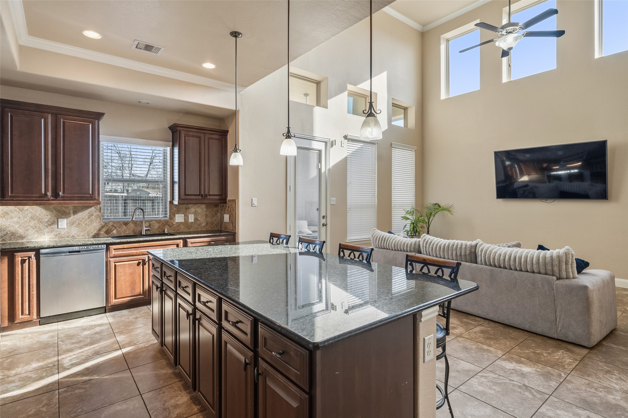 4747 Abercorn Street Rosharon, TX 77583 - Photo 14 of 46 This photo showcases a bright, open-concept kitchen and living area. It features a large kitchen island with granite countertops, dark wood cabinetry, and stainless steel appliances. The living space includes high ceilings, large windows, and a ceiling fan, providing a modern and inviting atmosphere.