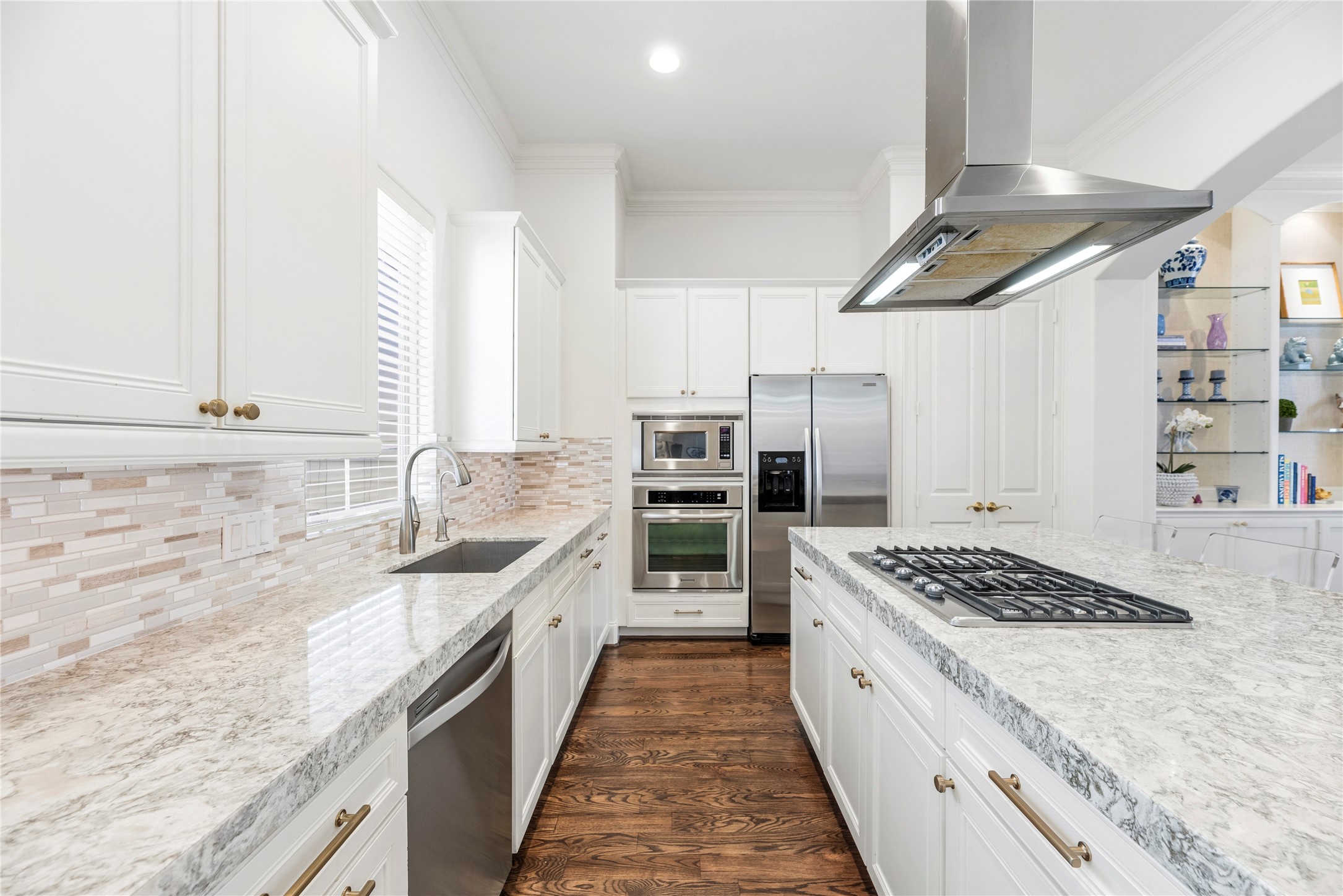 1537 Haddon Street Houston, TX 77006 - Photo 19 of 48 This kitchen features elegant white cabinetry, granite countertops, and a modern tile backsplash. It includes stainless steel appliances, a built-in oven, and a gas cooktop on the island, complemented by hardwood flooring and ample natural light.