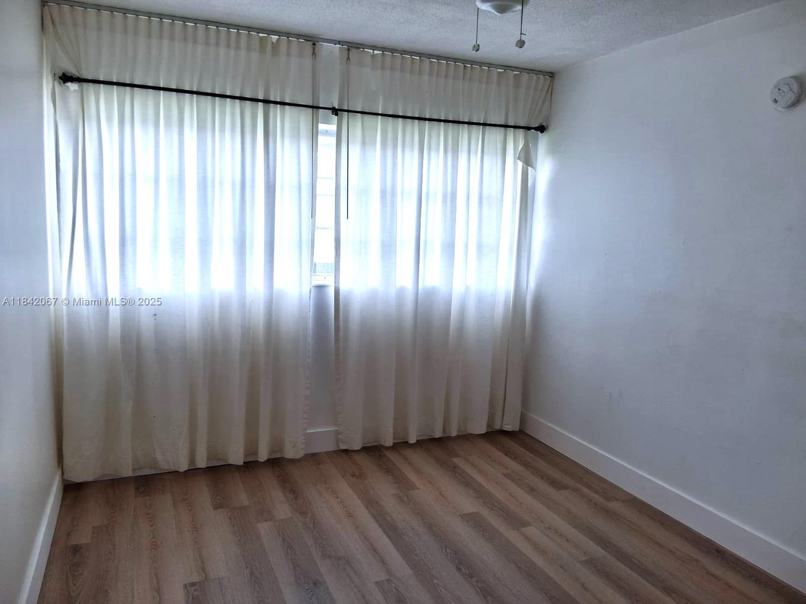 16801 Northeast 14th Avenue, Unit 209 Miami, FL 33162 - Photo 11 of 28 an empty room with wooden floor and windows