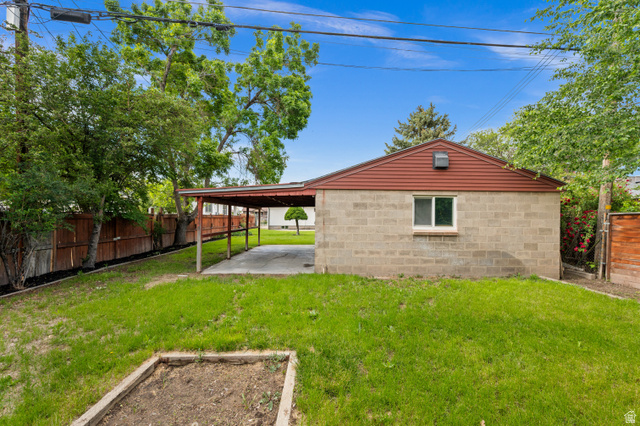 189 West Center Street Midvale, UT 84047 - Photo 54 of 64 Expansive backyard featuring a concrete block structure with a red gable roof, an attached carport, and mature perimeter trees