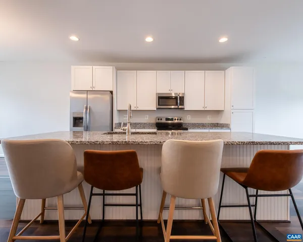 a kitchen with stainless steel appliances granite countertop a dining table chairs and a refrigerator