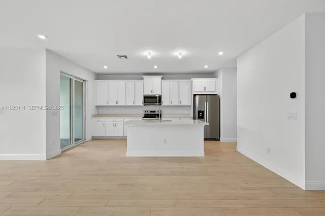 a large white kitchen with stainless steel appliances kitchen island a stove a refrigerator a sink and a stove