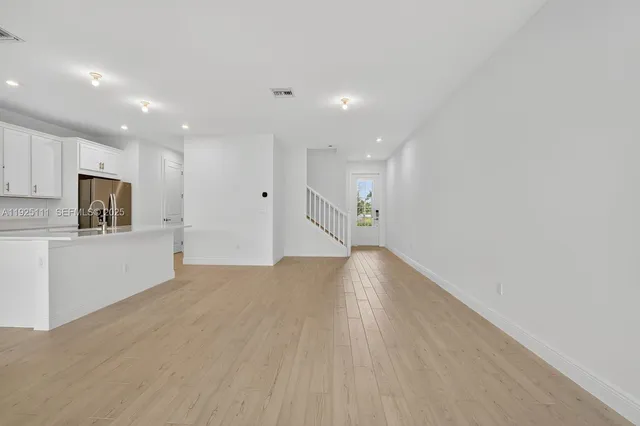 a view of empty room with wooden floor and kitchen