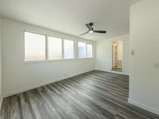 an empty room with wooden floor ceiling fan and window