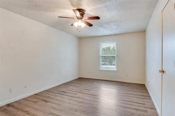 an empty room with wooden floor chandelier fan and windows