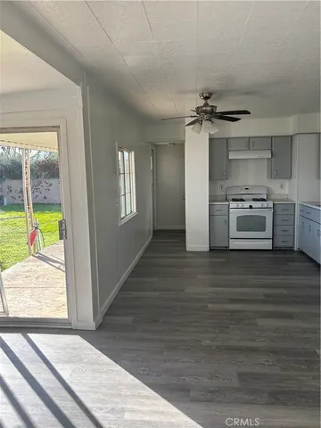 an empty room with wooden floor kitchen view and a window