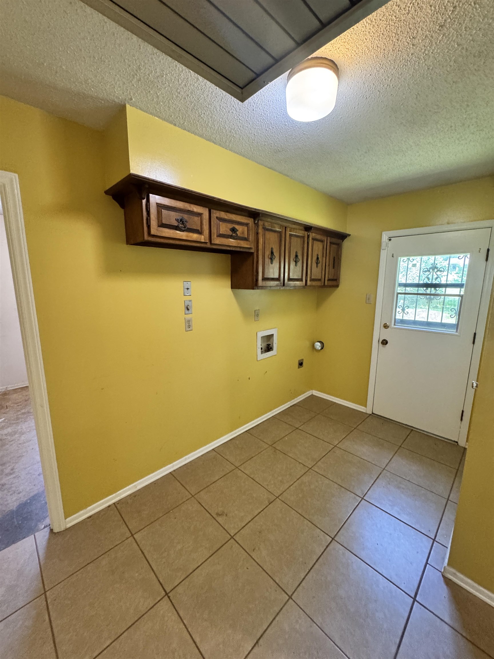 5520 Wagon Rd Gap, Unit GAP Memphis, TN 38134 - Photo 9 of 19 Utility room featuring ceramic tile flooring, wood cabinetry with decorative hardware, a ceiling-mounted light fixture, and a white exterior door with an integrated window and security bars