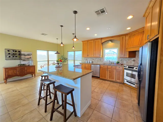 a kitchen with stainless steel appliances kitchen island granite countertop a table chairs and a refrigerator