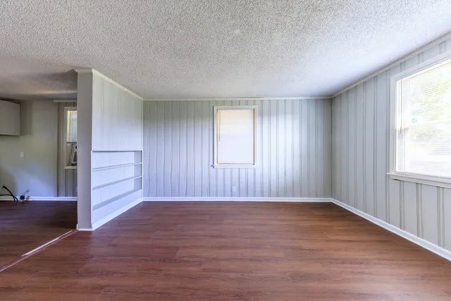 an empty room with wooden floor closet and windows