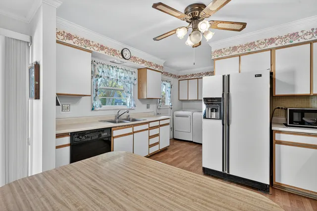 a large kitchen with a refrigerator a sink dishwasher a stove and white cabinets with wooden floor