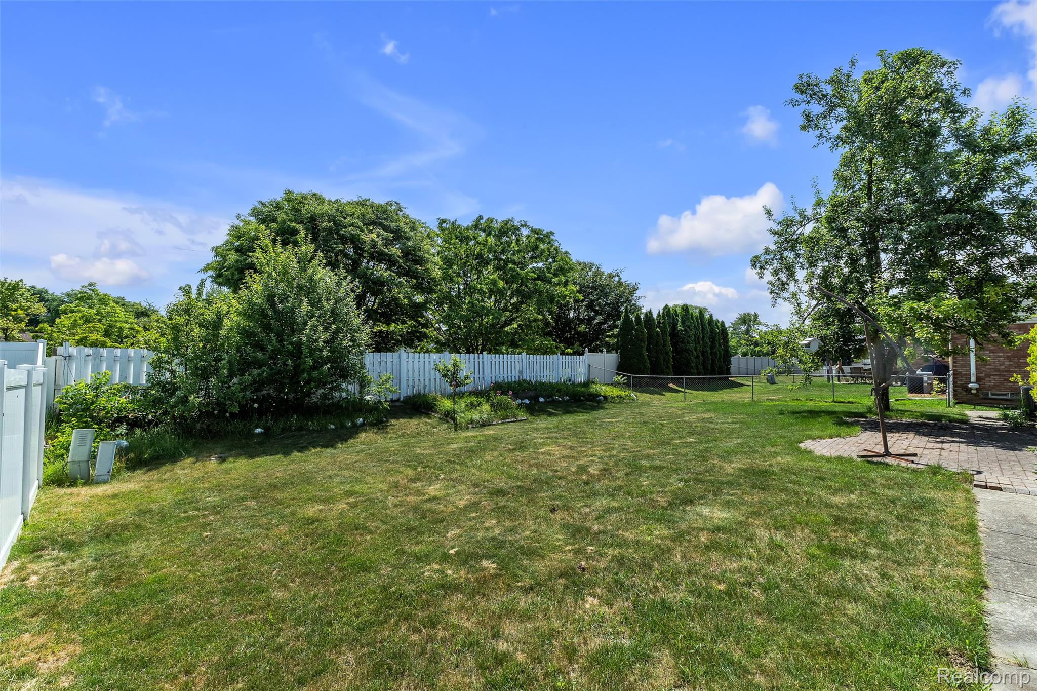 7000 Woonsocket Street Canton, MI 48187 - Photo 64 of 65 Expansive backyard featuring a large grass lawn, white privacy fencing, mature trees, and a brick paver patio area