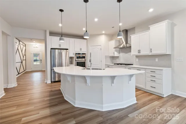 a large kitchen with stainless steel appliances kitchen island granite countertop a stove a refrigerator a oven and a wooden floors