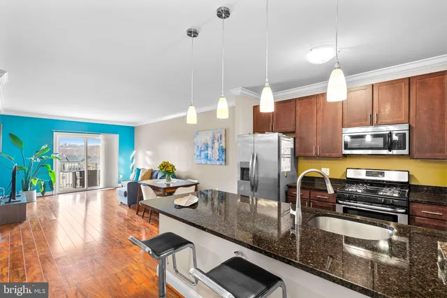 a kitchen with stainless steel appliances granite countertop a refrigerator a sink dishwasher a oven a dining table and chairs with wooden floor