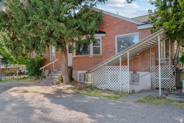 1275 North Geneva Road Provo, UT 84601 - Photo 11 of 25 Brick exterior with a mature tree, concrete steps with handrail, and a covered side entrance featuring lattice screening