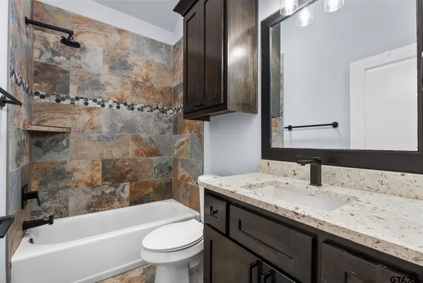 a bathroom with a granite countertop sink a toilet a mirror and shower