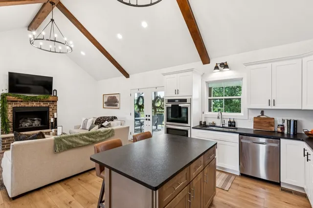 a living room with stainless steel appliances kitchen island granite countertop furniture a fireplace a flat screen tv and a window