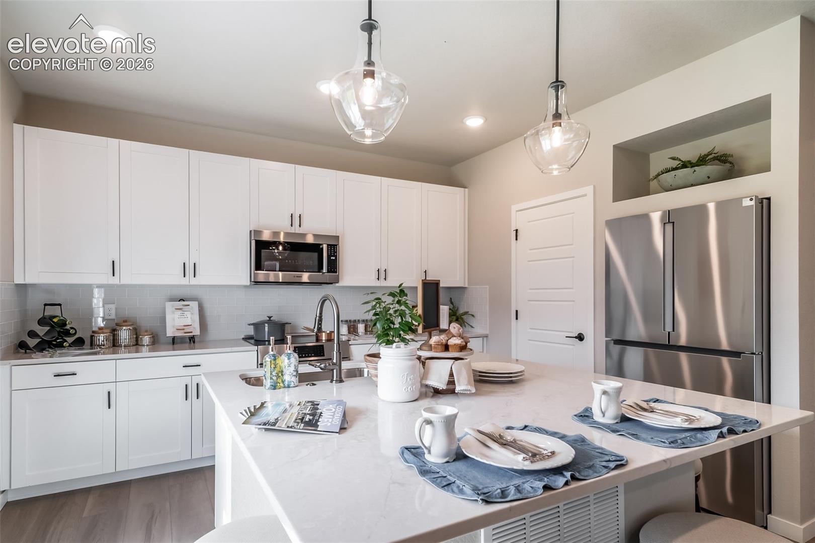 4876 Truscott Road Colorado Springs, CO 80925 - Photo 18 of 28 Gourmet kitchen featuring a large island with seating, stainless steel appliances, white shaker cabinetry, recessed lighting, and a subway tile backsplash
*Photos of a model home*