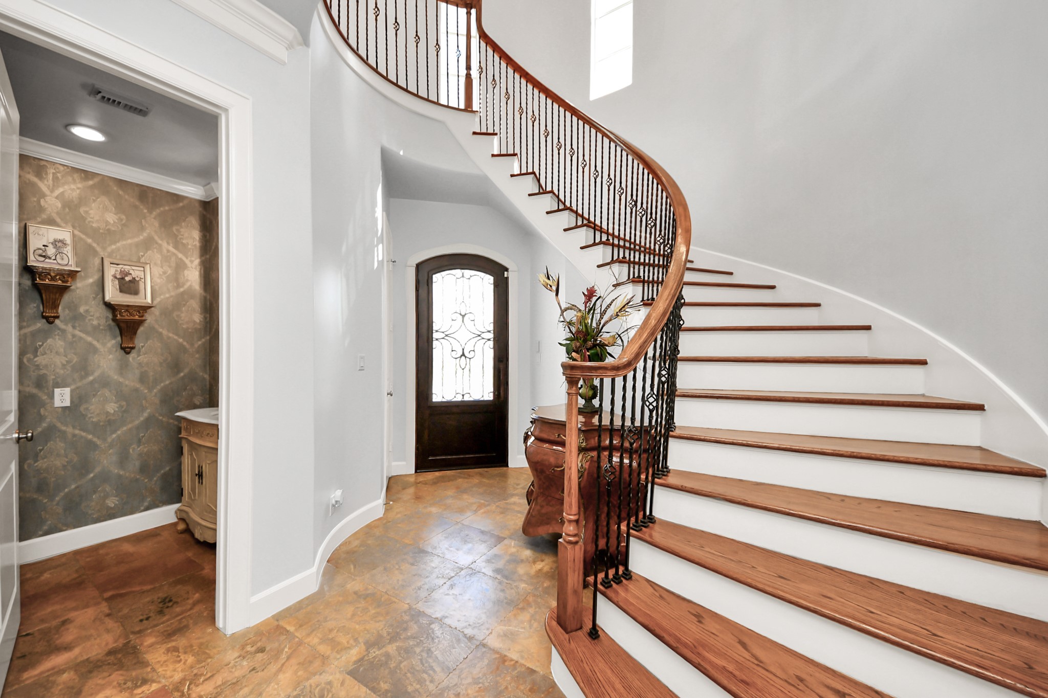 6302 Hermann Lake Drive Houston, TX 77021 - Photo 7 of 50 A sweeping staircase with rich wood handrails and modern metal balusters gracefully curves upward beneath soaring ceilings, creating a dramatic architectural moment.