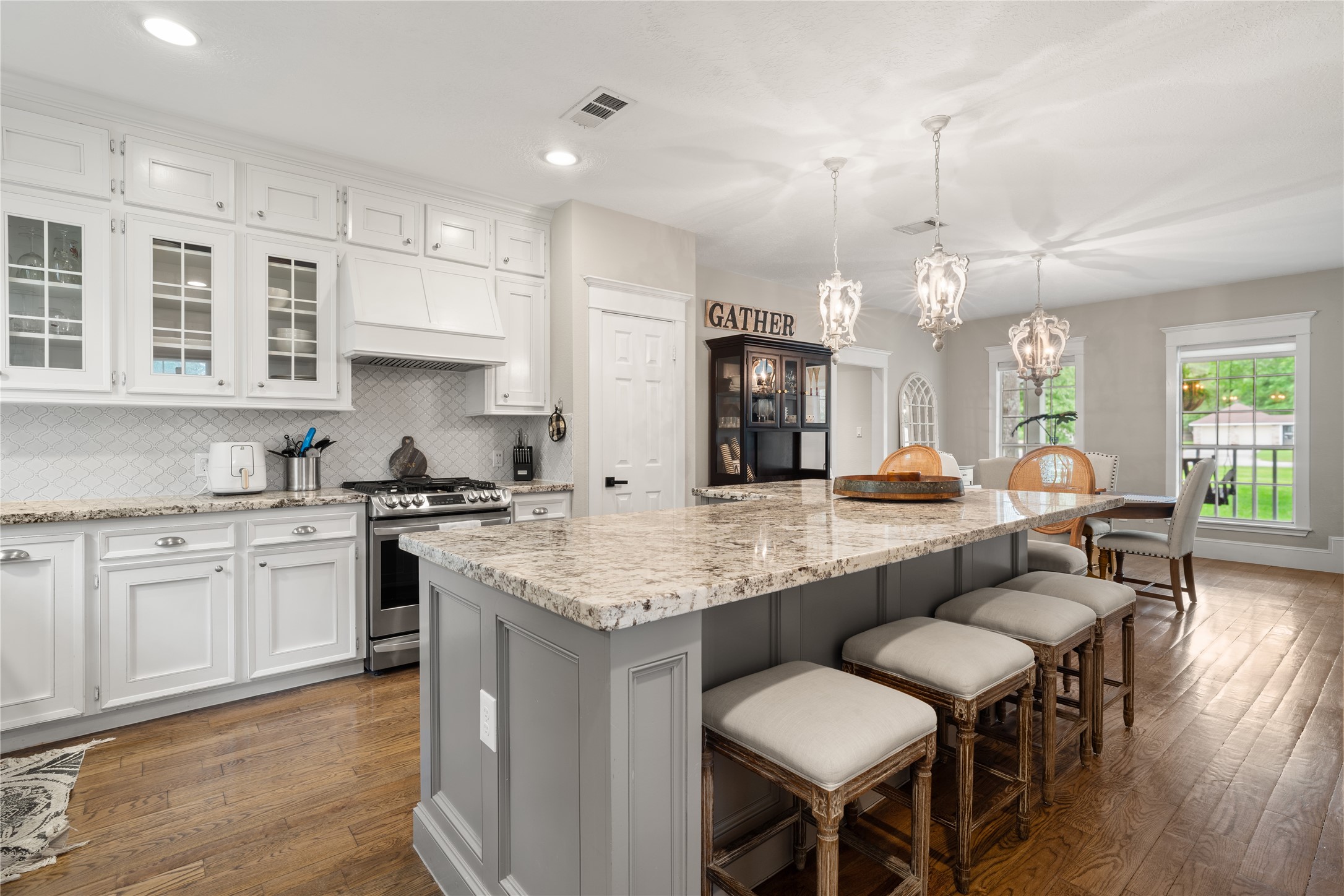 36 Wind River Drive Conroe, TX 77384 - Photo 20 of 45 This inviting kitchen features elegant white cabinetry, a large granite island with seating, stainless steel appliances, and chic pendant lighting. The open layout flows into a cozy dining area with large windows, offering plenty of natural light and a view of the outdoors.