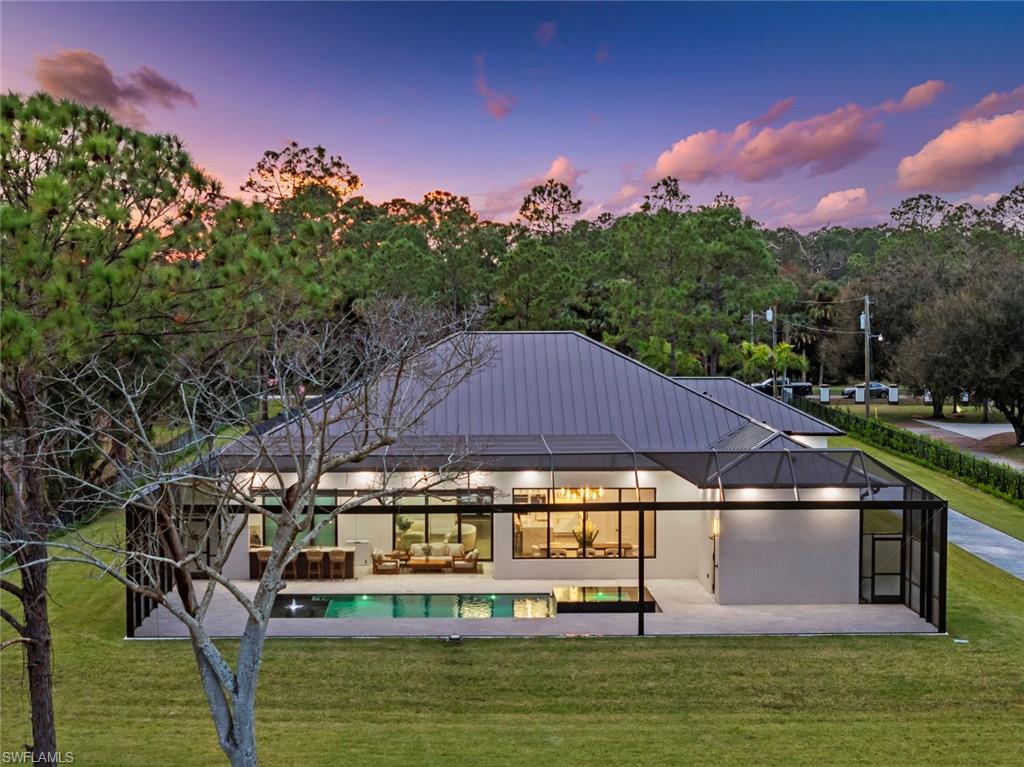 722 19th Street Southwest Naples, FL 34117 - Photo 5 of 47 Back house at dusk with an outdoor living space, a patio area, a lawn, and glass enclosure
