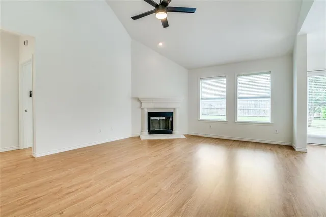 an empty room with wooden floor chandelier fan and windows