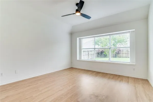 an empty room with wooden floor ceiling fan and windows