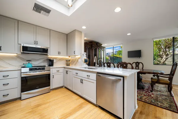 a kitchen with stainless steel appliances granite countertop a stove top oven a sink dishwasher and white cabinets next to a window