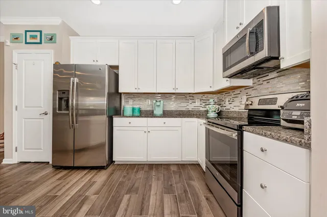 a kitchen with stainless steel appliances granite countertop a refrigerator oven a sink dishwasher and white cabinets with wooden floor