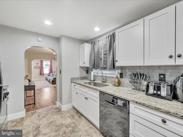 a kitchen with a sink dishwasher a stove and white cabinets with wooden floor