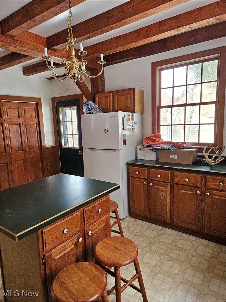 Kitchen with dark countertops, freestanding refrigerator, light floors, a center island, and beamed ceiling