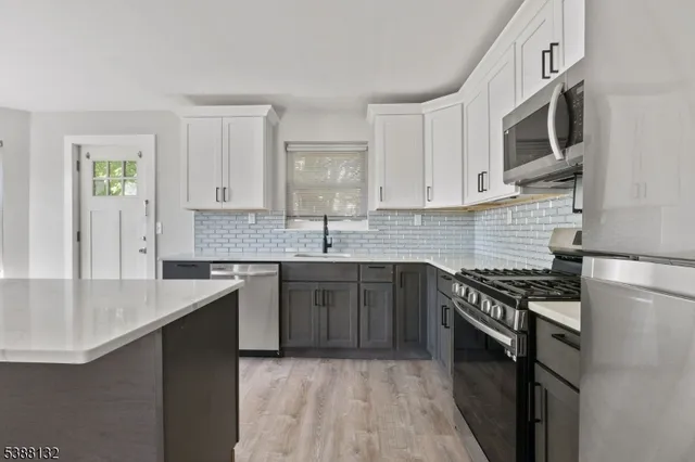 a kitchen with stainless steel appliances granite countertop a stove top oven a sink dishwasher and a microwave oven with white cabinets