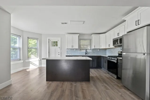 a kitchen with stainless steel appliances granite countertop a refrigerator a sink dishwasher a stove and white countertops with wooden floor