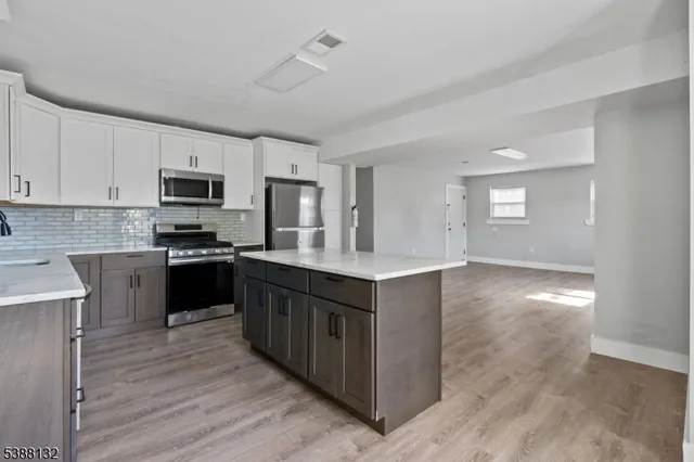 a kitchen with granite countertop a refrigerator oven a sink dishwasher and white cabinets with wooden floor