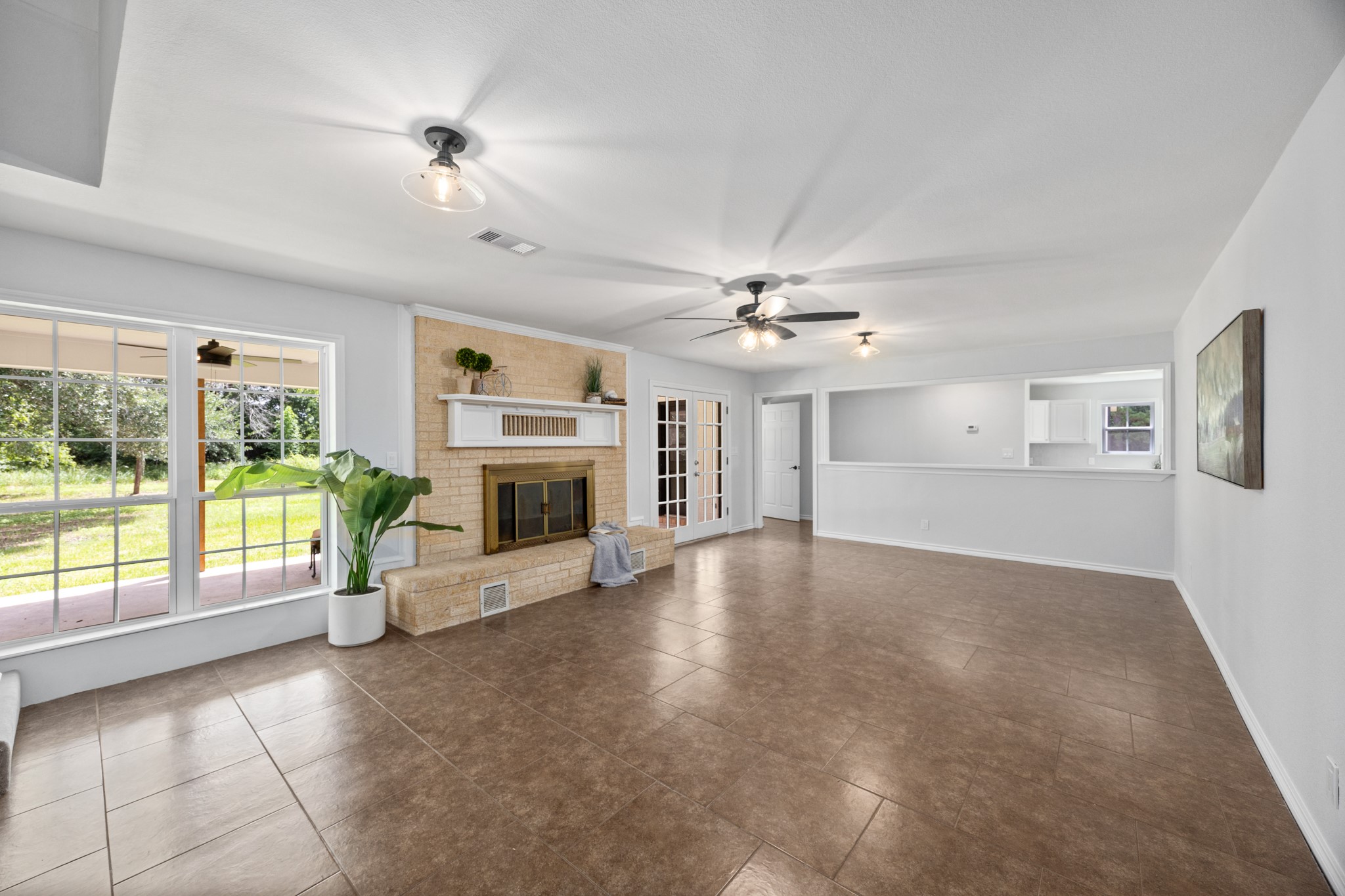 10209 Oberrender Road Needville, TX 77461 - Photo 13 of 50 This spacious living room features a cozy fireplace with a mantel, tile flooring, and large windows offering plenty of natural light. The room opens to a bright kitchen area, and there's a ceiling fan for comfort.