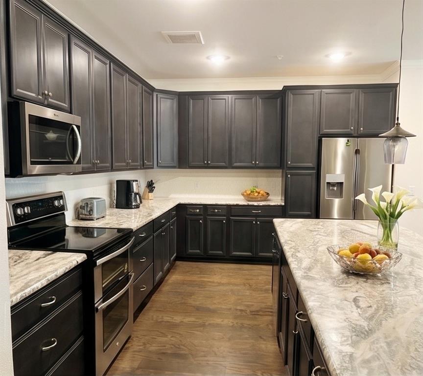 651 Watters Road, Unit 8204 Allen, TX 75013 - Photo 1 of 11 Kitchen featuring dark wood-finish cabinetry, light-toned countertops, stainless steel appliances, a kitchen island, and wood-finish flooring