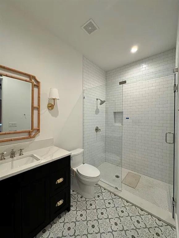 5800 Goodwin Avenue Dallas, TX 75206 - Photo 21 of 39 Bathroom featuring a dark vanity with a light countertop, a toilet, and a glass-enclosed shower with subway tile