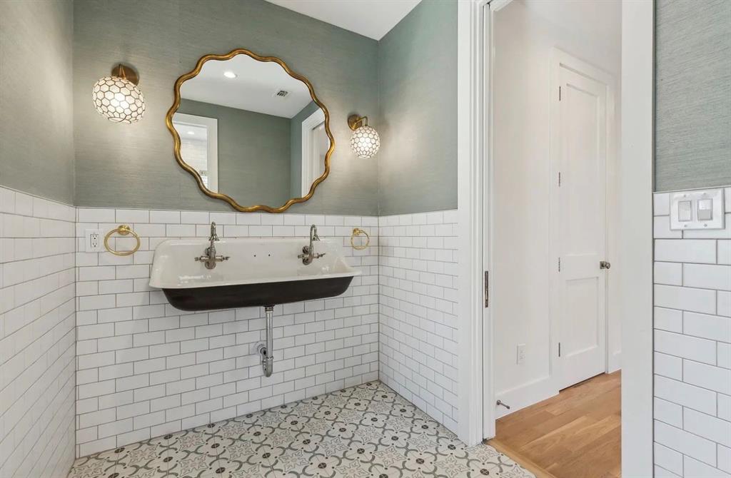 5800 Goodwin Avenue Dallas, TX 75206 - Photo 35 of 39 Bathroom featuring white subway tile wainscoting, patterned floor tiles, a gold-framed mirror, and a double-basin sink