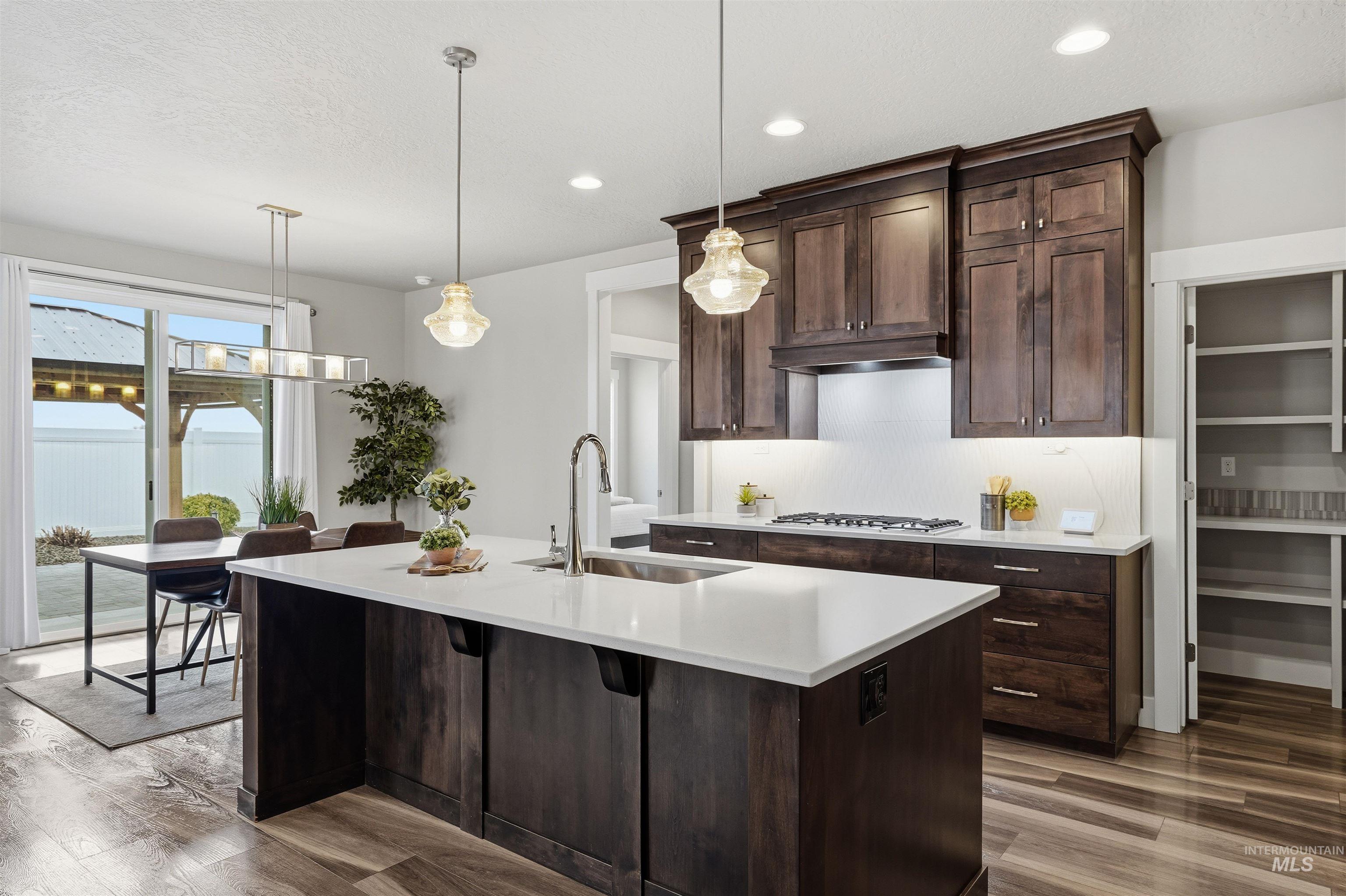 8087 Tandy Cove Street Middleton, ID 83644 - Photo 12 of 50 Kitchen with dark wood finish cabinetry, hanging light fixtures, a center island with sink, and dark wood-style flooring