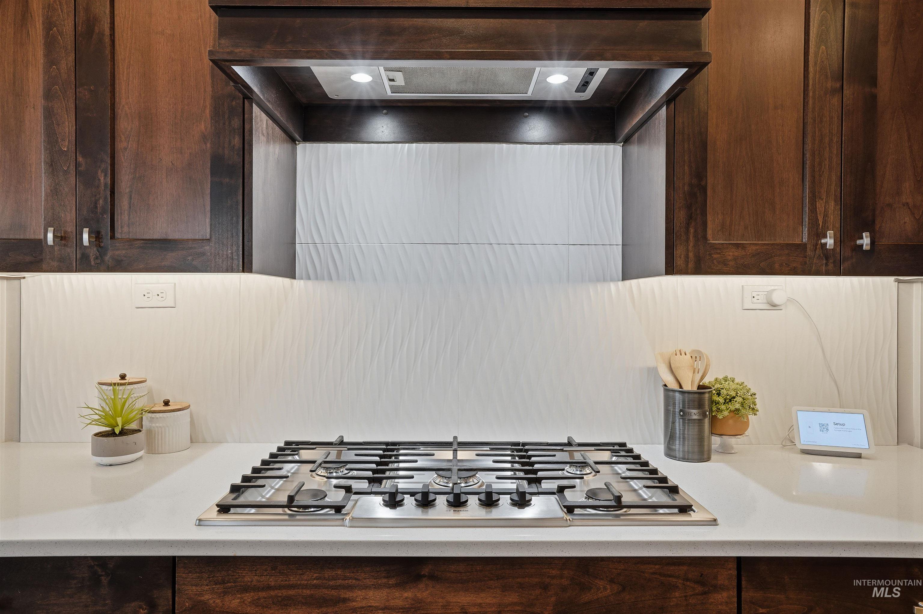8087 Tandy Cove Street Middleton, ID 83644 - Photo 14 of 50 Kitchen view of range hood, stainless steel gas stovetop, dark wood finish cabinets, and light stone counters