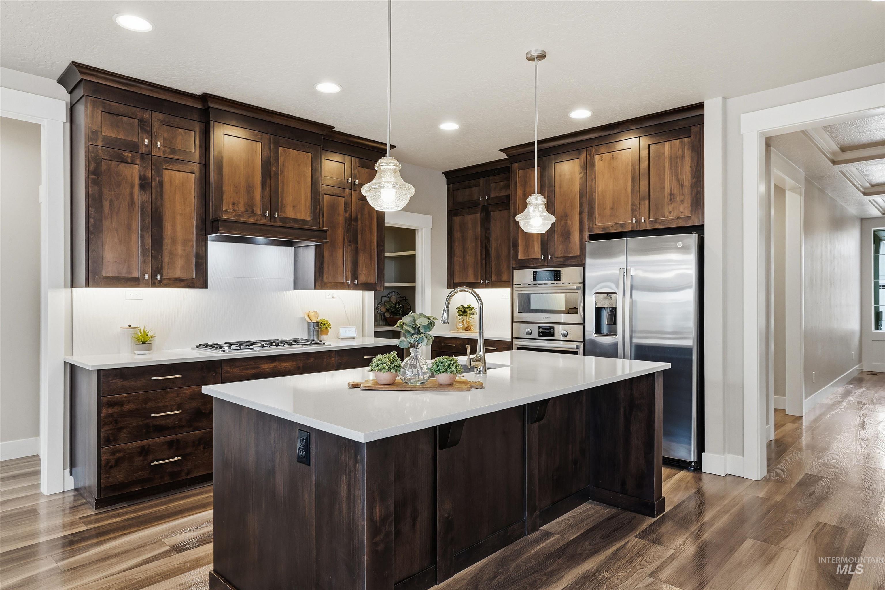 8087 Tandy Cove Street Middleton, ID 83644 - Photo 14 of 50 Kitchen with stainless steel appliances, dark wood finish cabinetry, hanging light fixtures, a kitchen island with sink, and dark wood-style floors