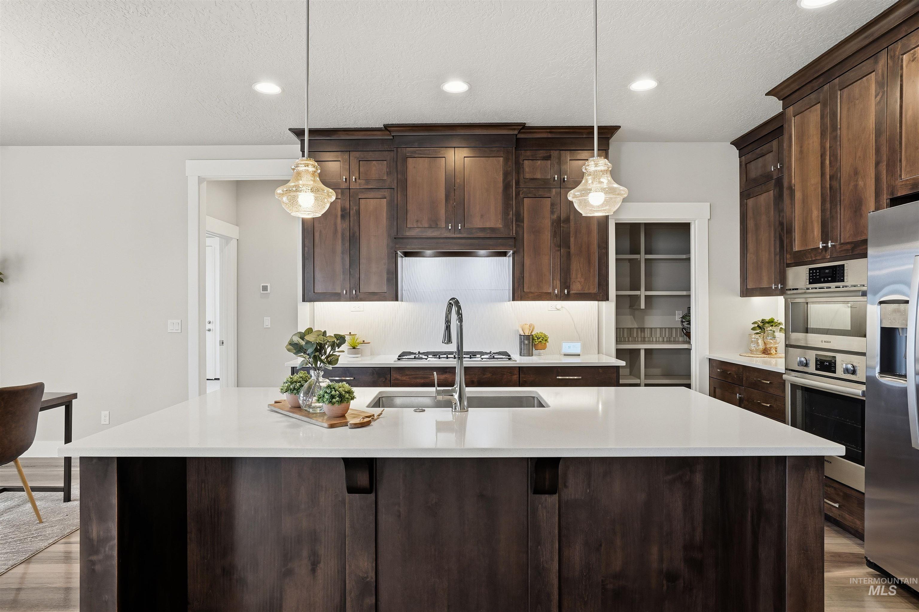 8087 Tandy Cove Street Middleton, ID 83644 - Photo 15 of 50 Kitchen with dark wood finish cabinetry, hanging light fixtures, light wood finished floors, and a textured ceiling