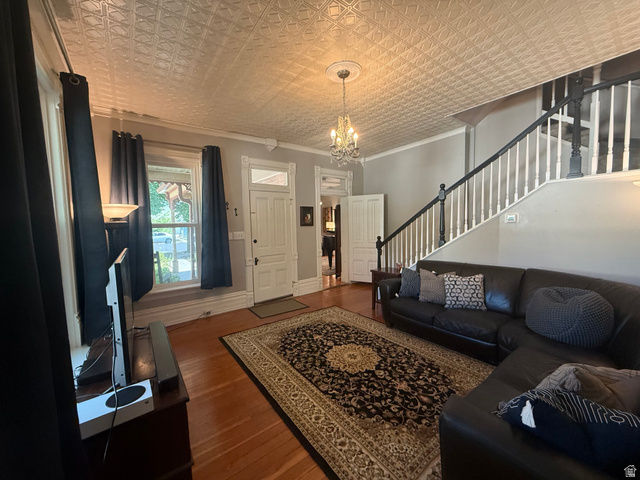 541 300 North Provo, UT 84606 - Photo 14 of 36 Living area featuring a detailed pressed tin ceiling, wood-finish flooring, a chandelier with a ceiling medallion, a staircase with white spindles and dark banister, and a paneled entry door