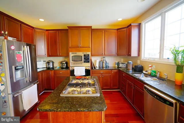 a kitchen with stainless steel appliances granite countertop a stove top oven a sink and dishwasher a refrigerator with wooden floor