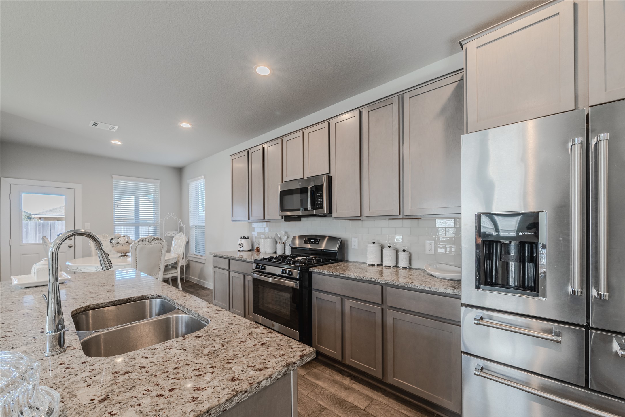 4259 Wyanngate Drive Spring, TX 77373 - Photo 14 of 46 Modern kitchen equipped with stainless steel appliances and elegant grey cabinetry, opening directly into a sunlit breakfast nook.