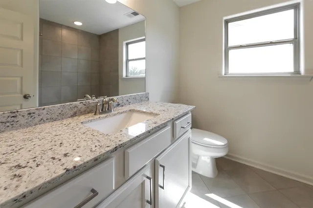 a bathroom with a granite countertop sink a toilet and a window