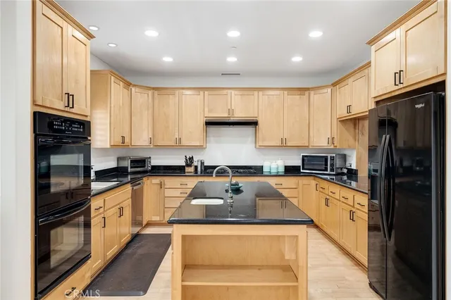 a kitchen with granite countertop a refrigerator a sink dishwasher a stove top oven a kitchen island and cabinets with wooden floor